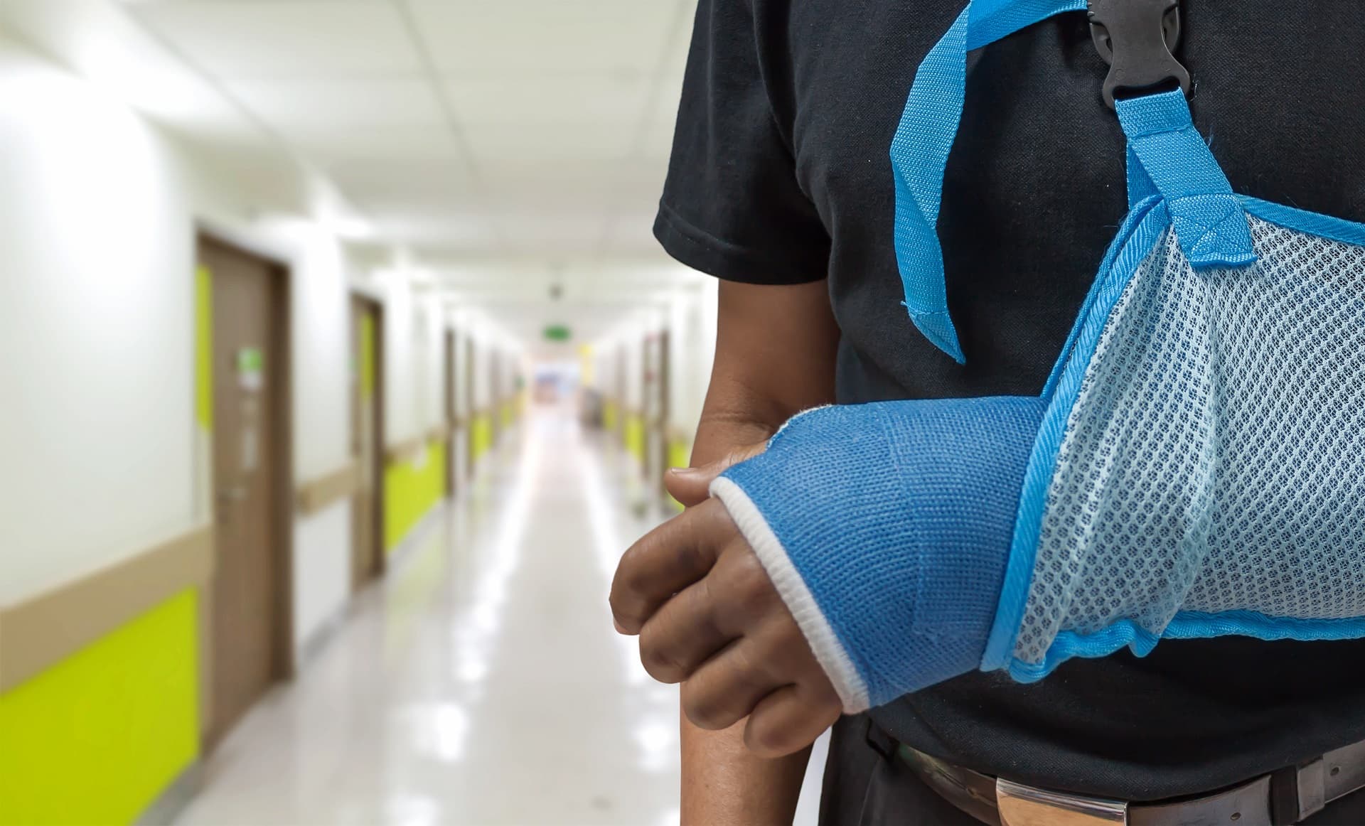 Man's arm in cast and sling with blurred hospital background