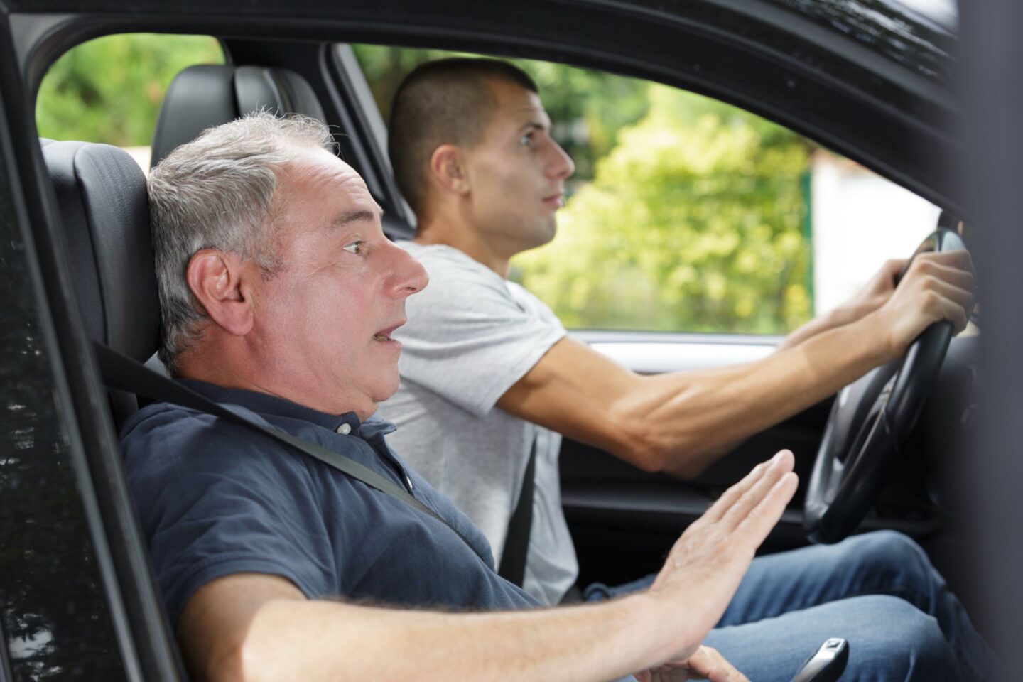 Two men sitting in the front seat of a vehicle one driving and one scared passenger