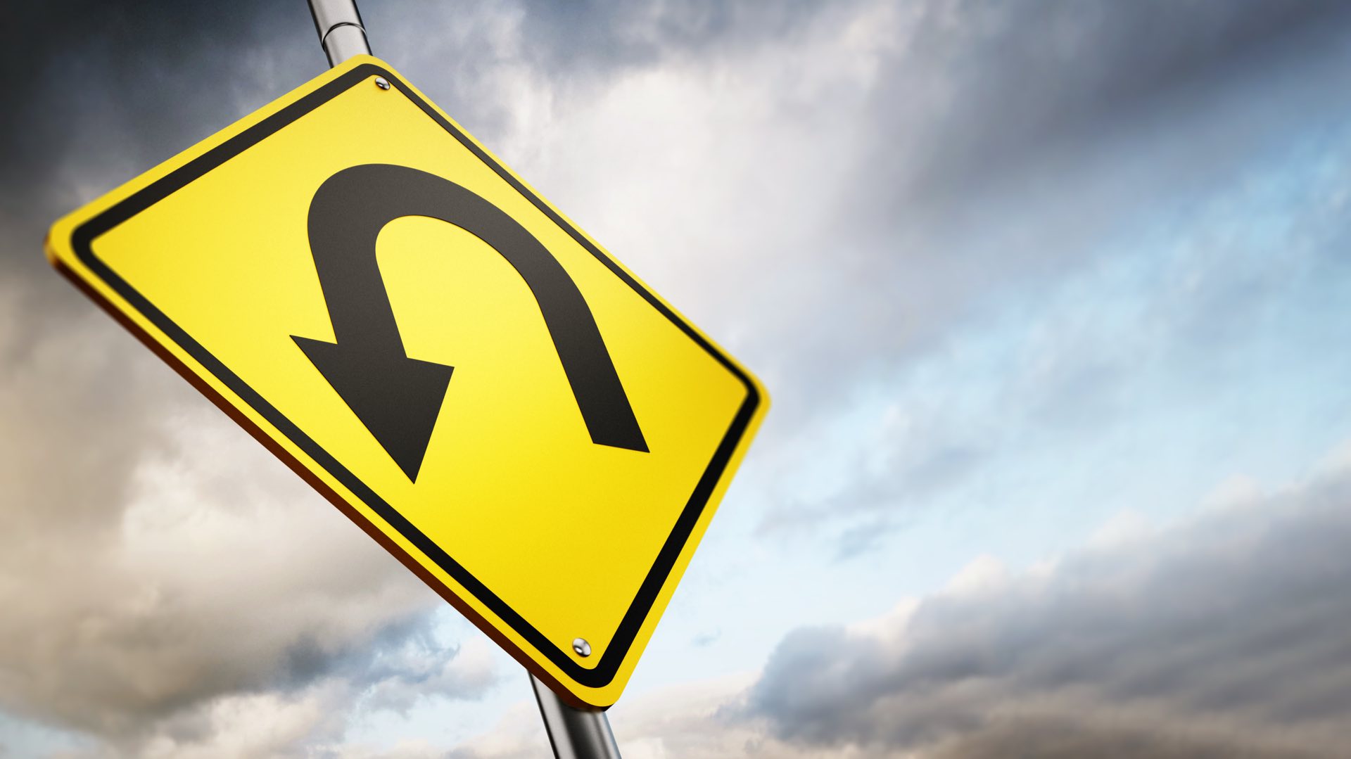 U turn road warning sign against a gloomy sky