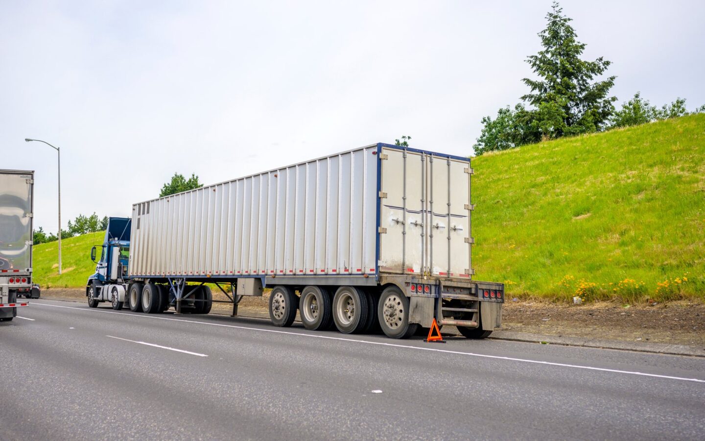 Big rig on the side of the road with an orange triangle at the back of it