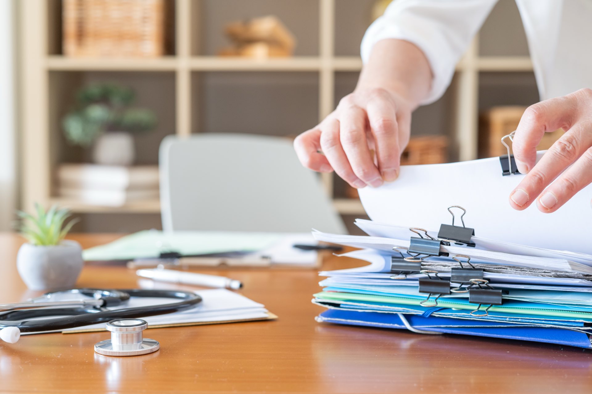 A person going through a stack of paperwork at a desk with a stethoscope on the table