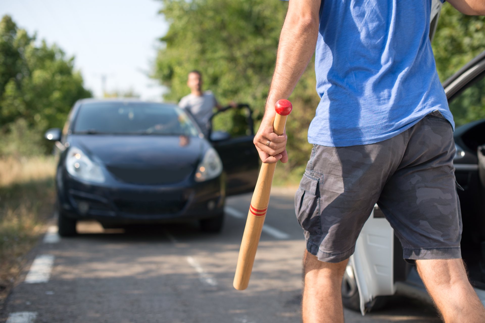 One person in a black car stopped and the other person getting out of their car with a bat in their hand