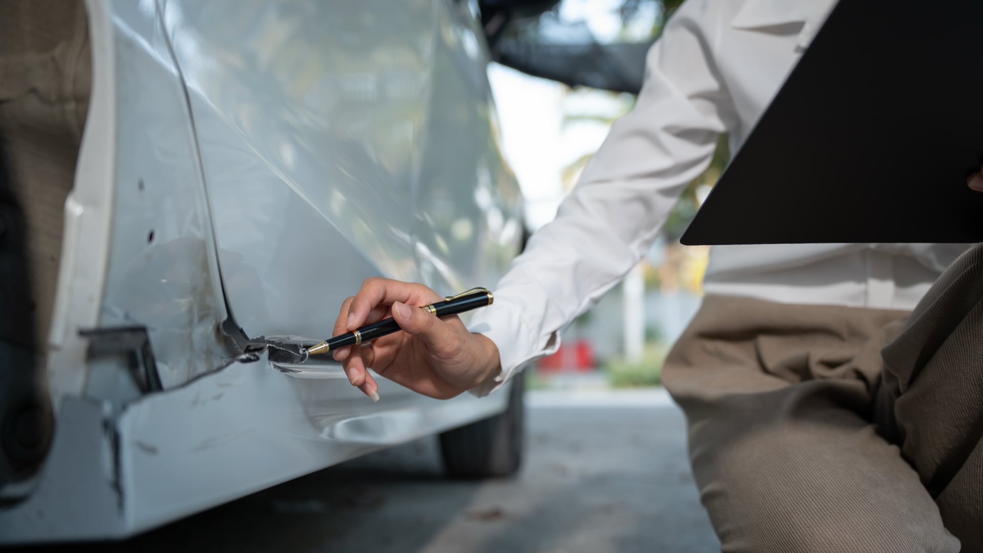 A while vehicle in an accident with a person looking at the damages holding a clipboard