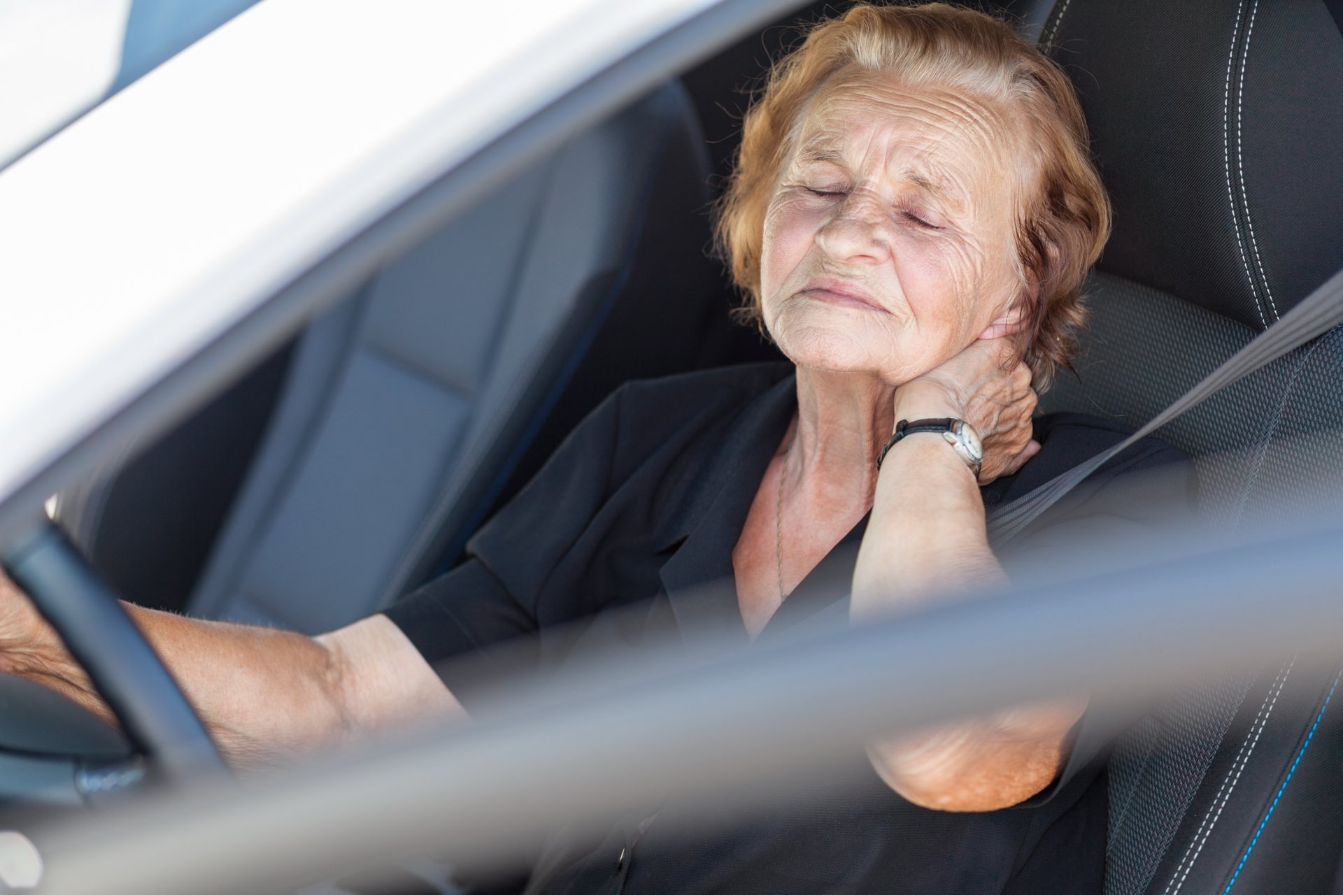 Elderly woman holding her neck in a vehicle