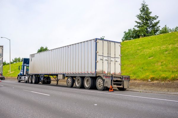 Big rig on the side of the road with an orange triangle at the back of it