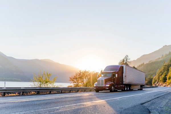Red semi truck driving by mountain lake | truck accident lawyer | Henderson Taylor Law Firm