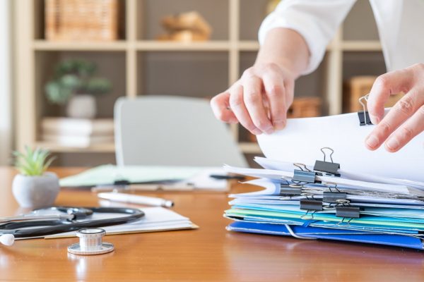 A person going through a stack of paperwork at a desk with a stethoscope on the table