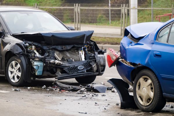 Side view. Front of dark and back of blue cars damaged and broken by accident on the road