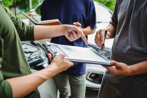 Three people discussing insurance paperwork on a clipboard