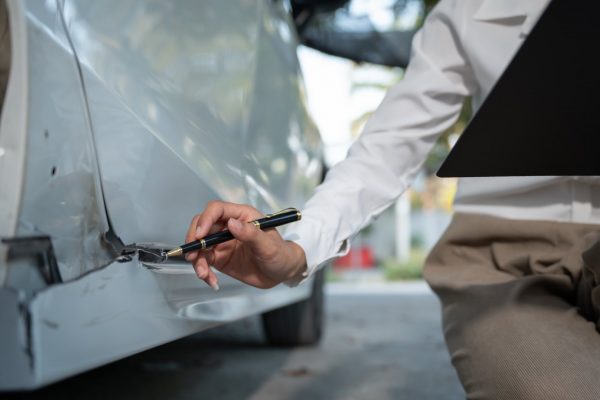 A while vehicle in an accident with a person looking at the damages holding a clipboard