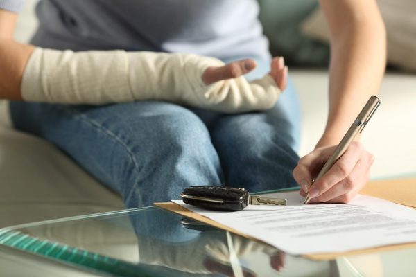 A woman with a broken arm writes on a piece of paper sitting on a couch next to a key fob.
